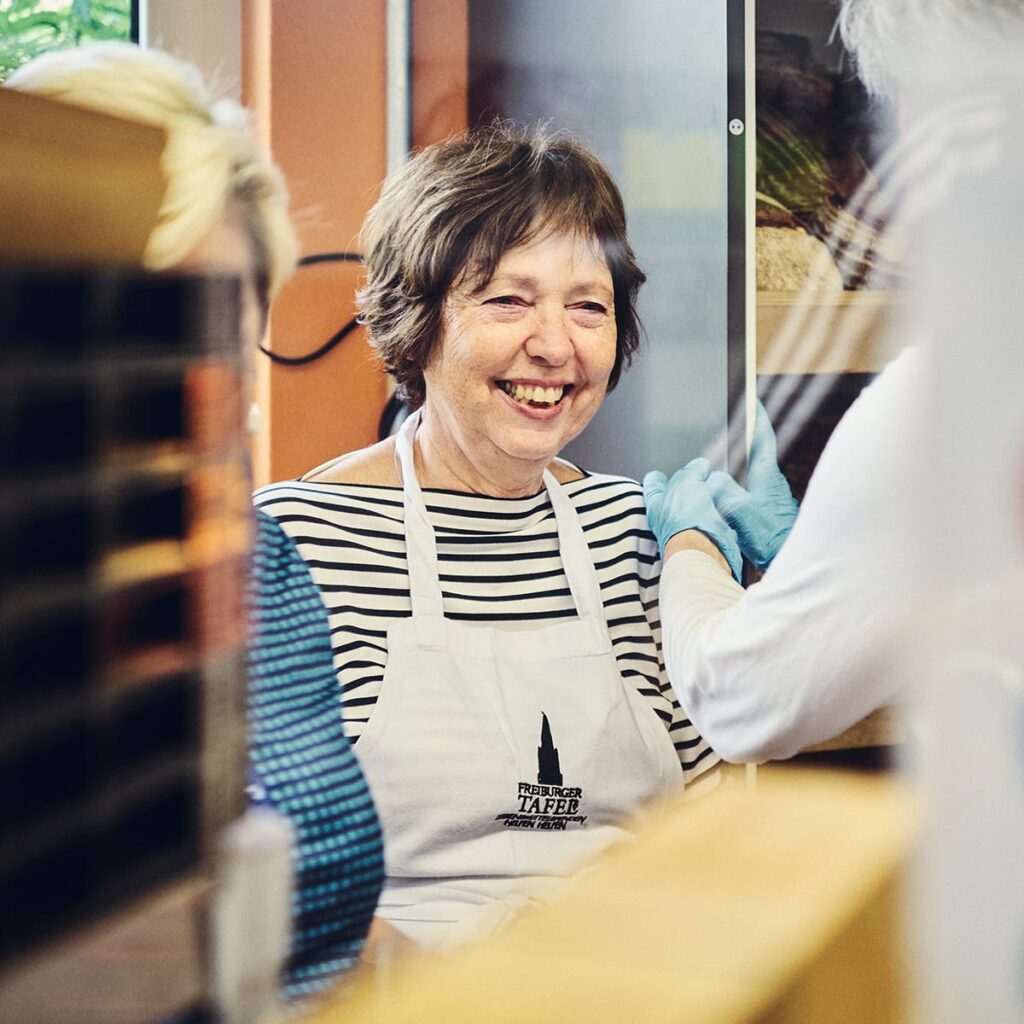 Eine Ehrenamtliche Frau steht lächelnd an der Backwarentheke im Laden.