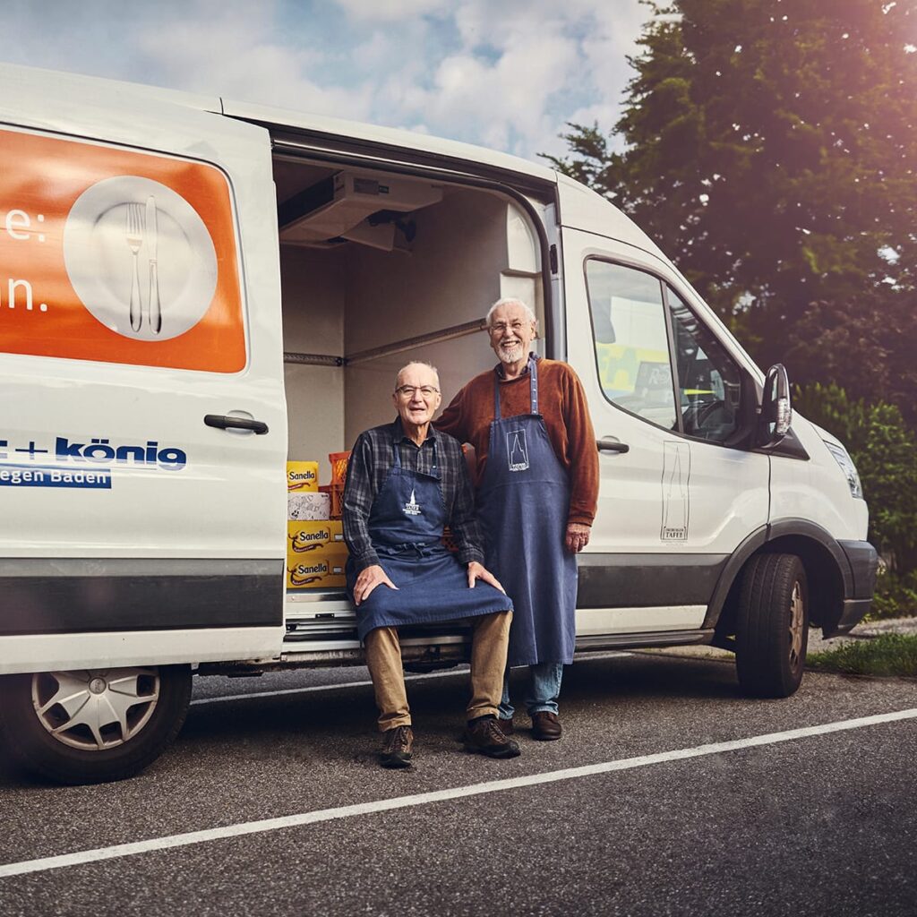 Zwei ehrenamtliche Fahrer vor einem geöffneten Lieferwagen.