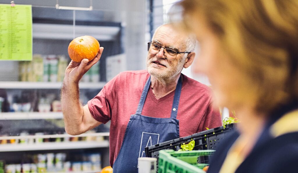 Ein Mann mit einer Schürze präsentiert durch Hochheben einen Kürbis.